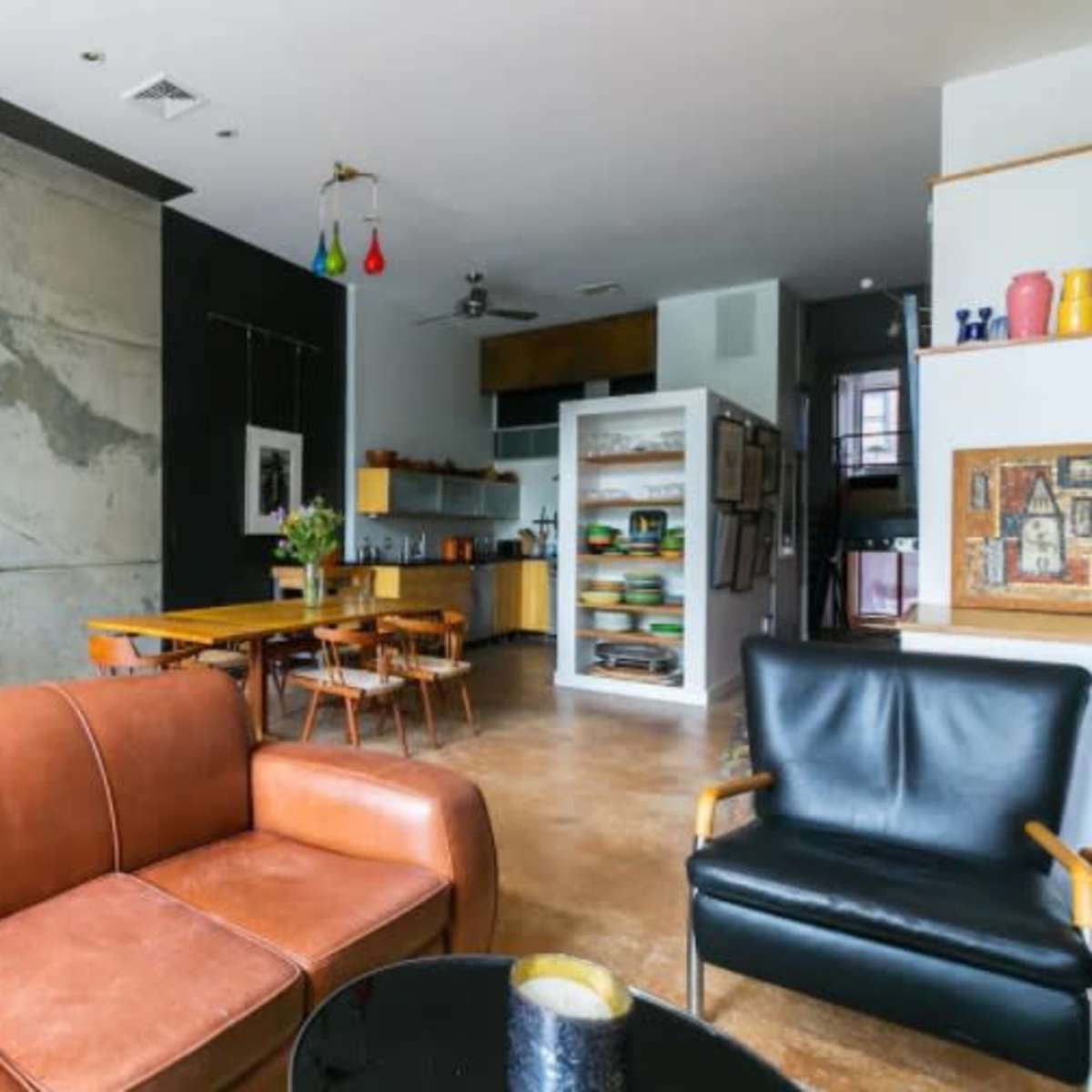 A modern living space with a concrete wall, wooden furniture, and a kitchenette in the background.