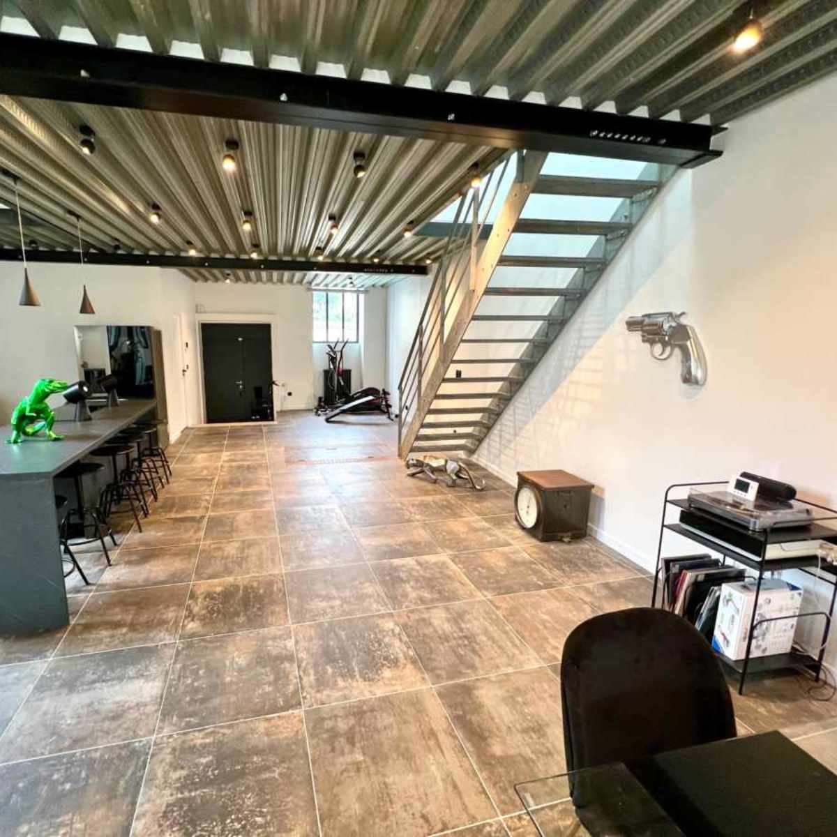 A spacious interior with a modern kitchen island, a green sculpture, and a staircase leading to an upper level.