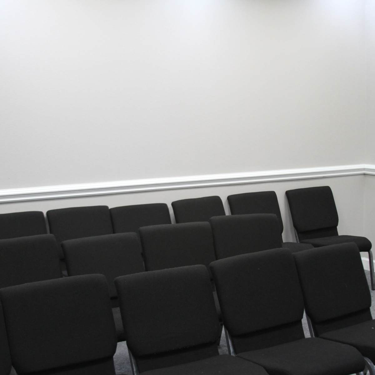A small meeting room with rows of black chairs facing a wall-mounted television.