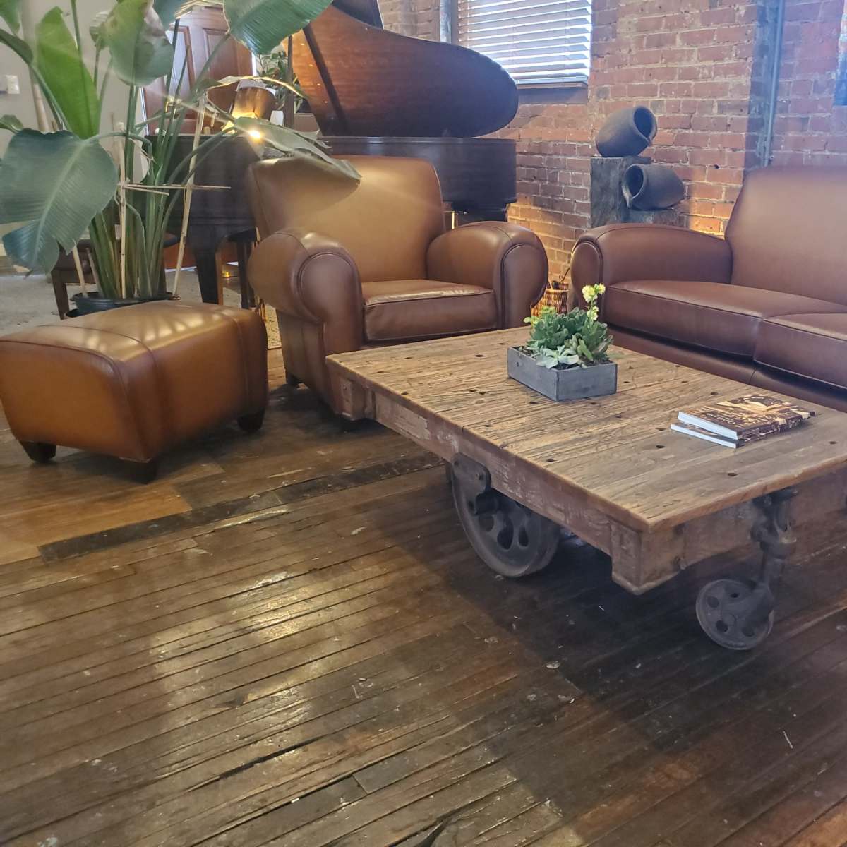 A living room with a leather sofa, a matching armchair, and a wooden coffee table with wheels, all arranged on a wooden floor.