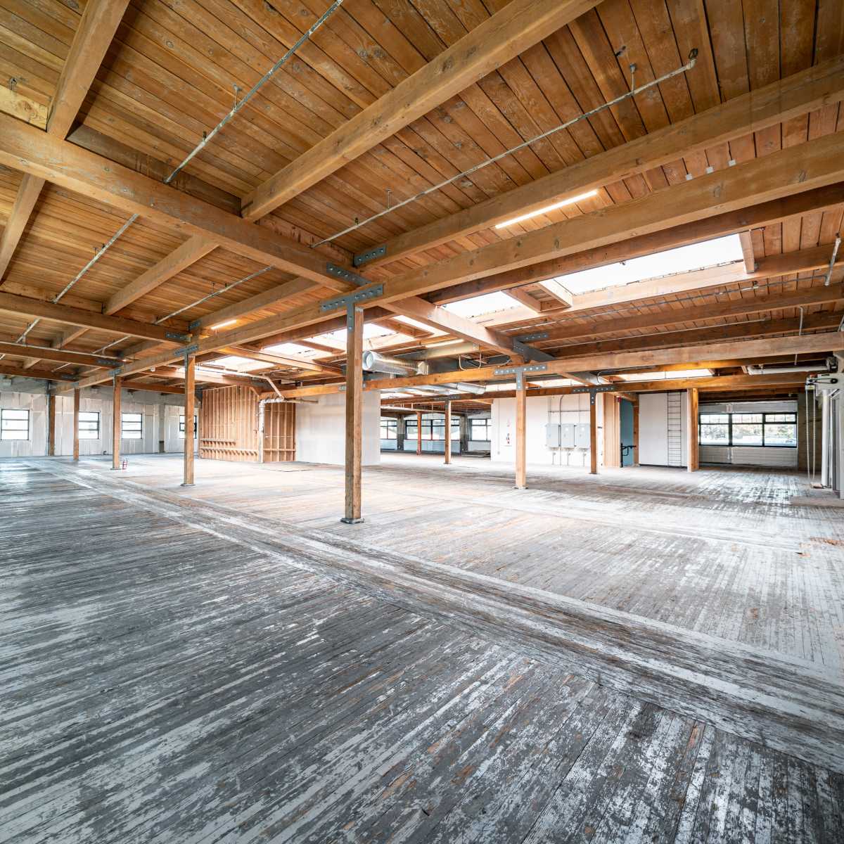 A spacious, empty interior of a building with exposed wooden beams and a wooden floor.