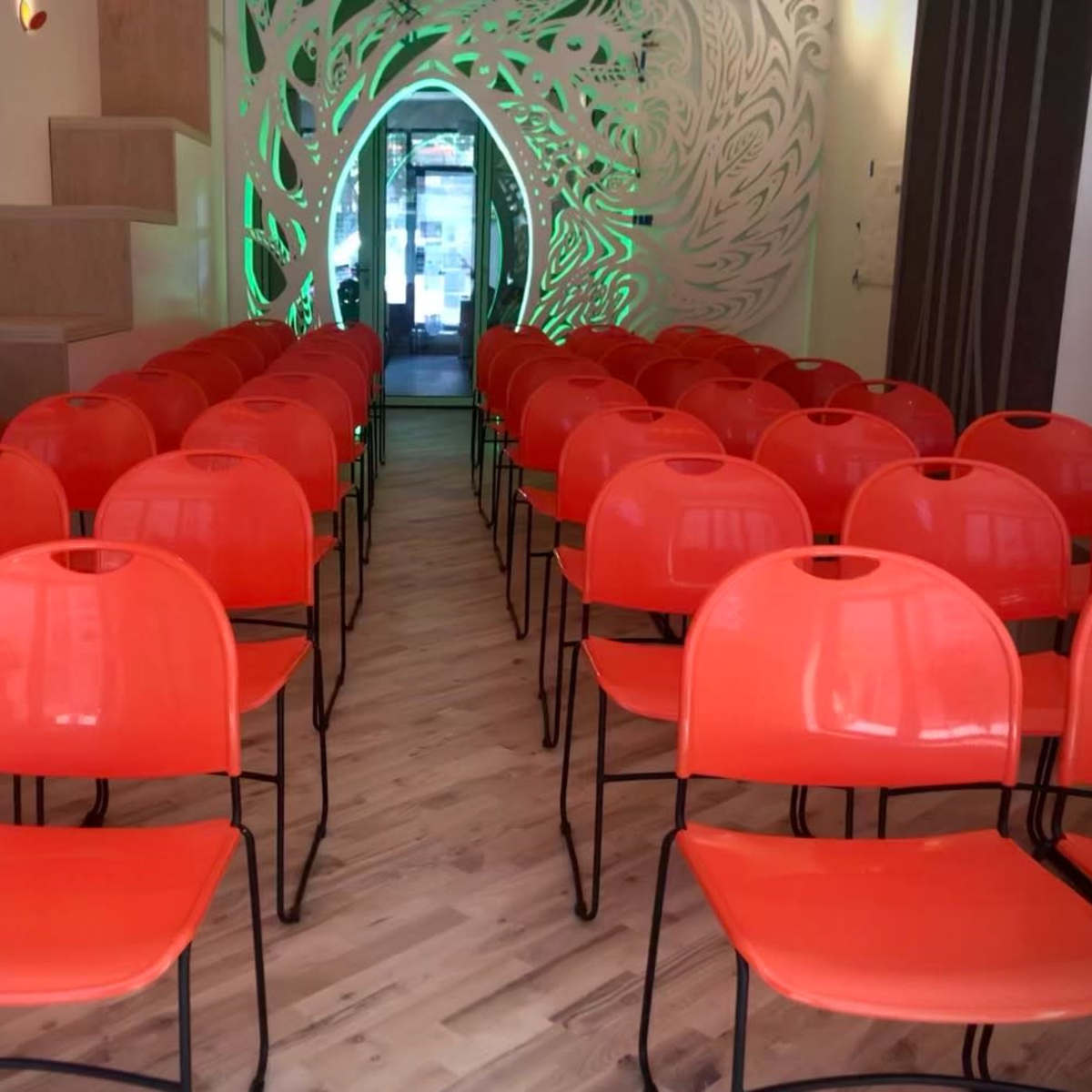 A room with rows of orange chairs arranged neatly facing a doorway adorned with decorative designs.