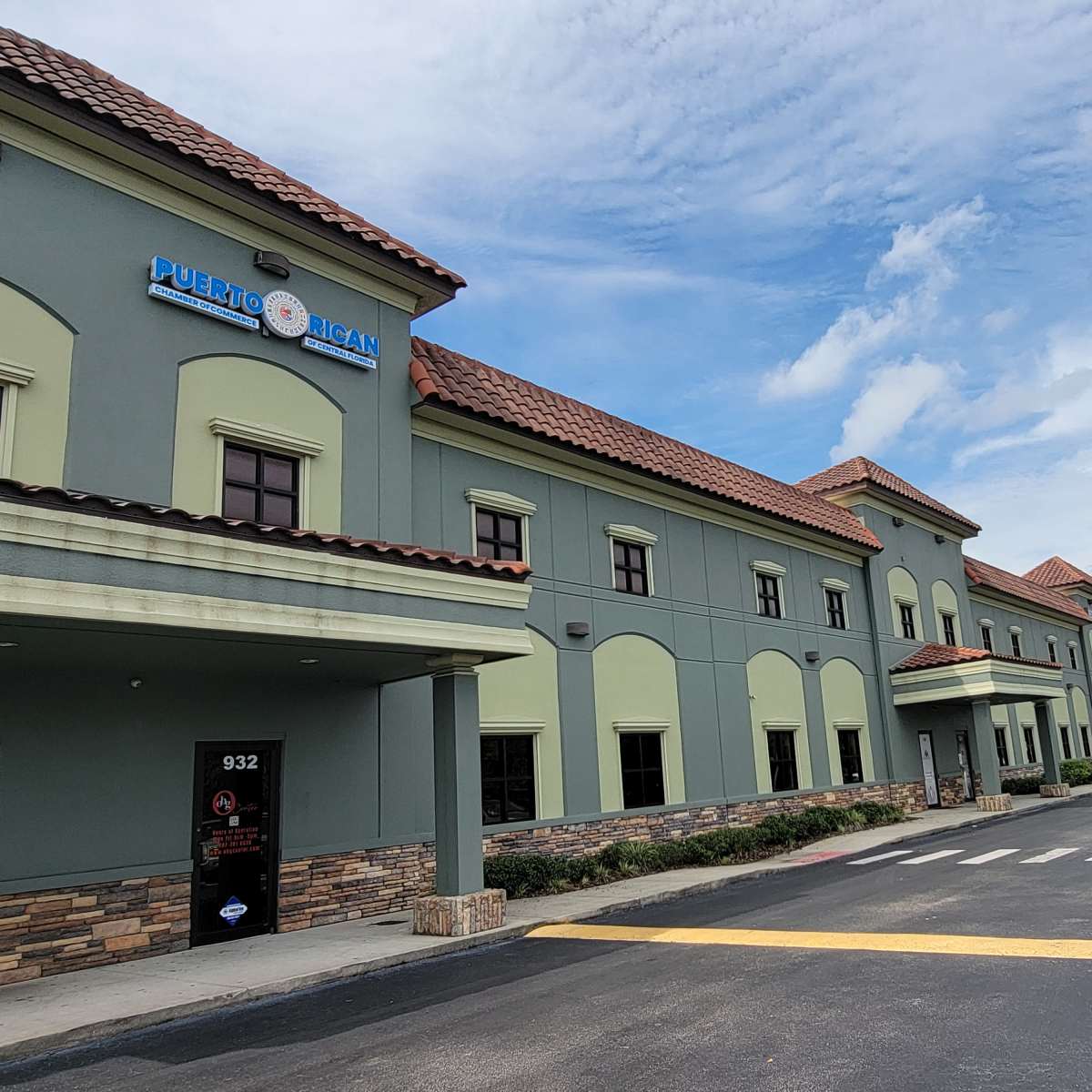 A green and beige building with a red tile roof, featuring signage for a Puerto Rican restaurant and a parking lot in front.