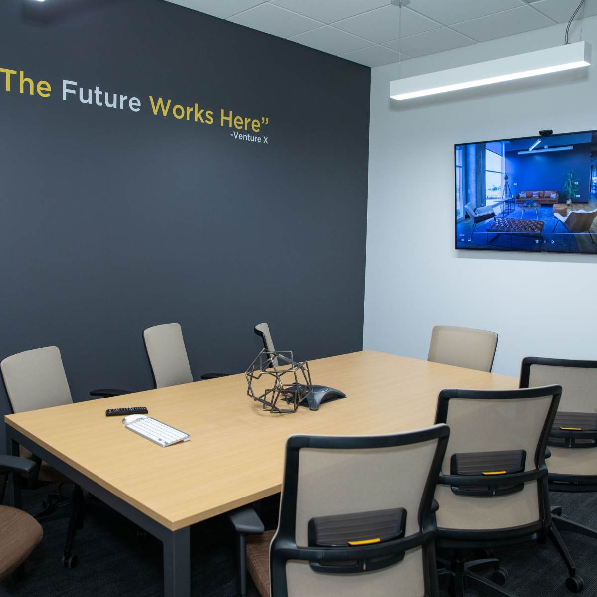A conference room features a table surrounded by chairs, with a large screen displaying an image on the wall next to a quote about the future.