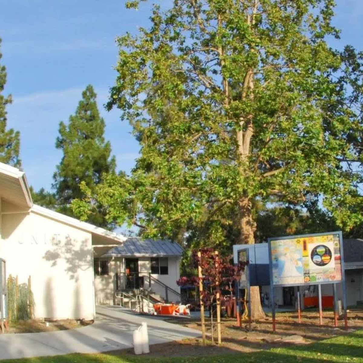 A modern building with large colorful windows, surrounded by green trees and a nearby information board.