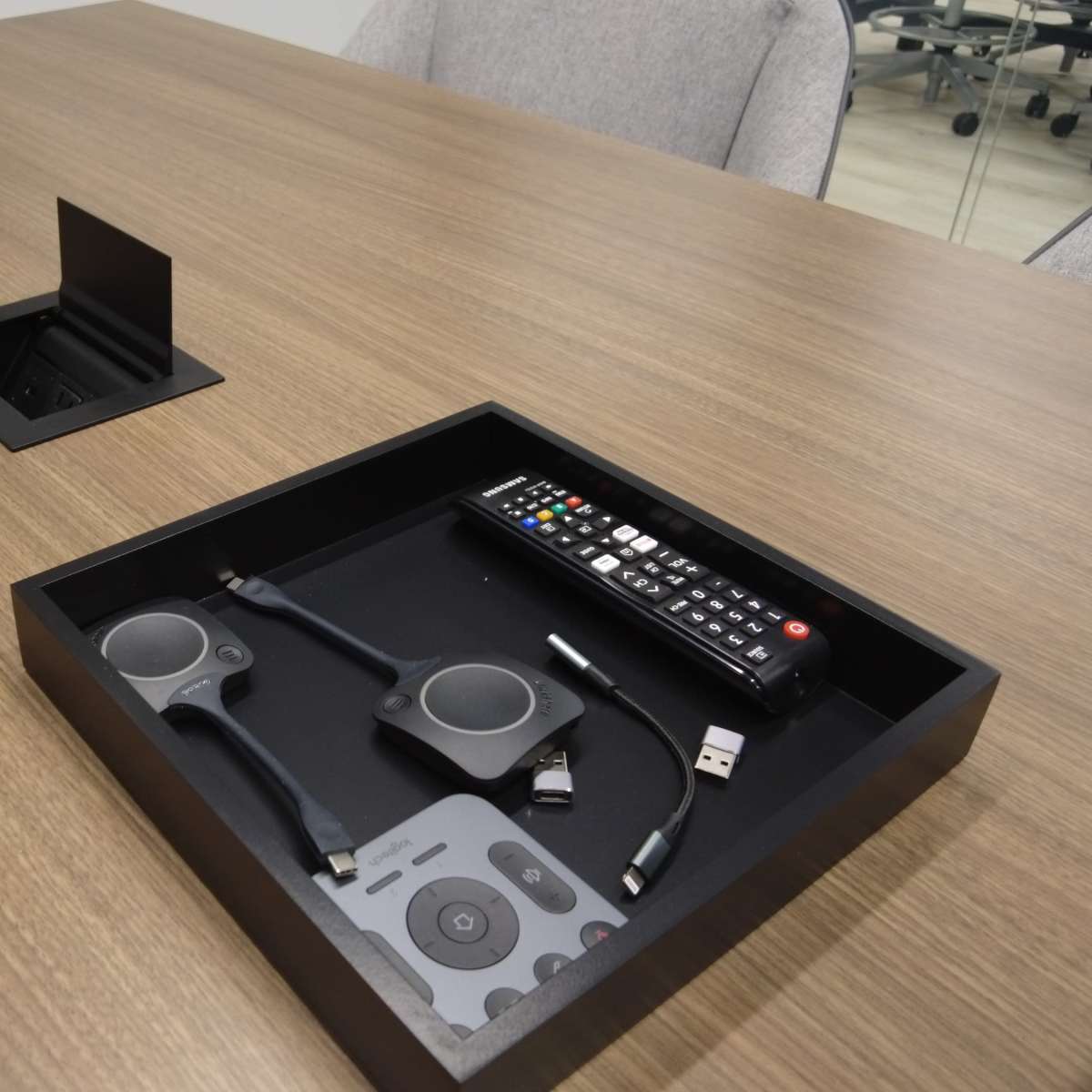 A conference table features a recessed box containing a remote control and various electronic cables.