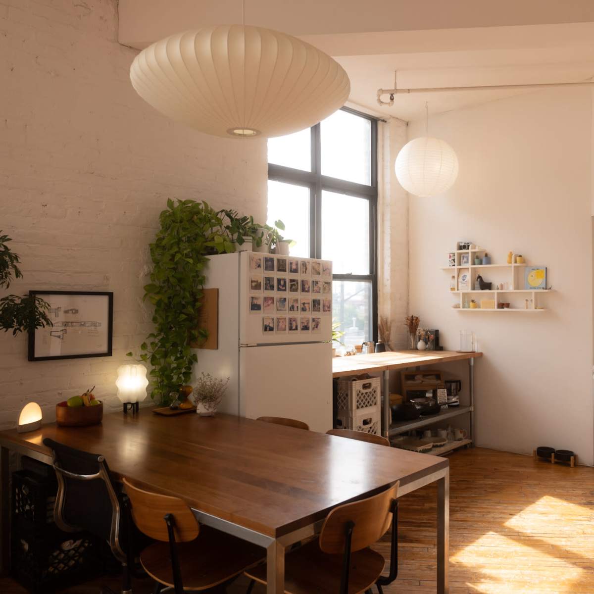 A bright kitchen with a wooden dining table, a refrigerator, and open shelves displaying various kitchen items.