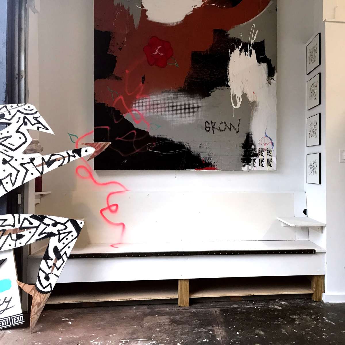 An art-filled room with a large abstract painting on the wall, a minimalist bench in front, and a bathroom door in the background.