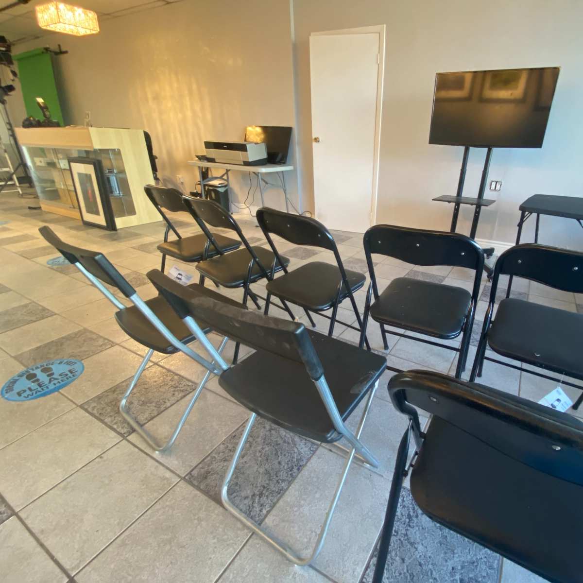 A set of black folding chairs is arranged in rows facing a television screen in a minimalistic room.