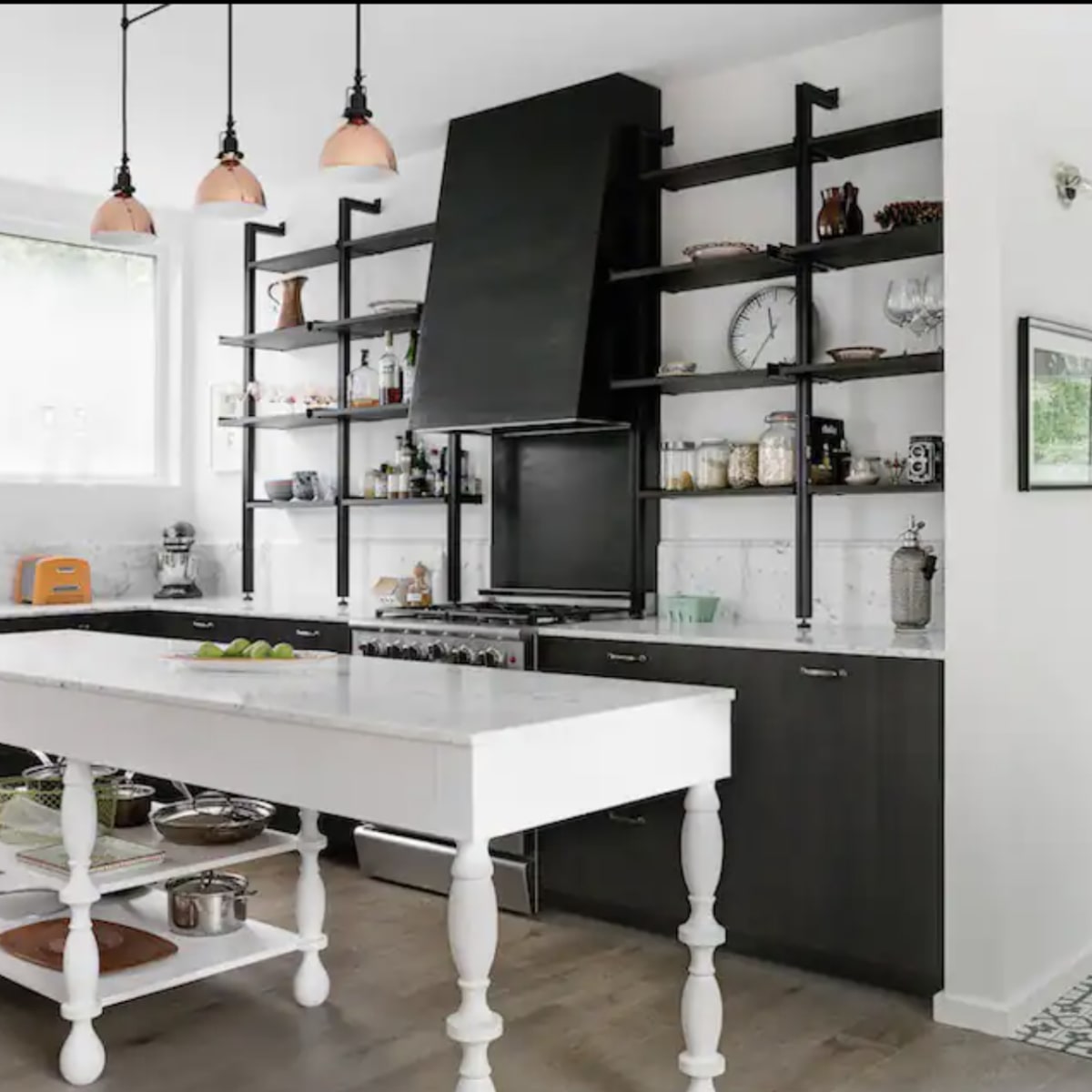 A modern kitchen with dark cabinetry, open shelving, and a central white island with a lower shelf displaying cookware.