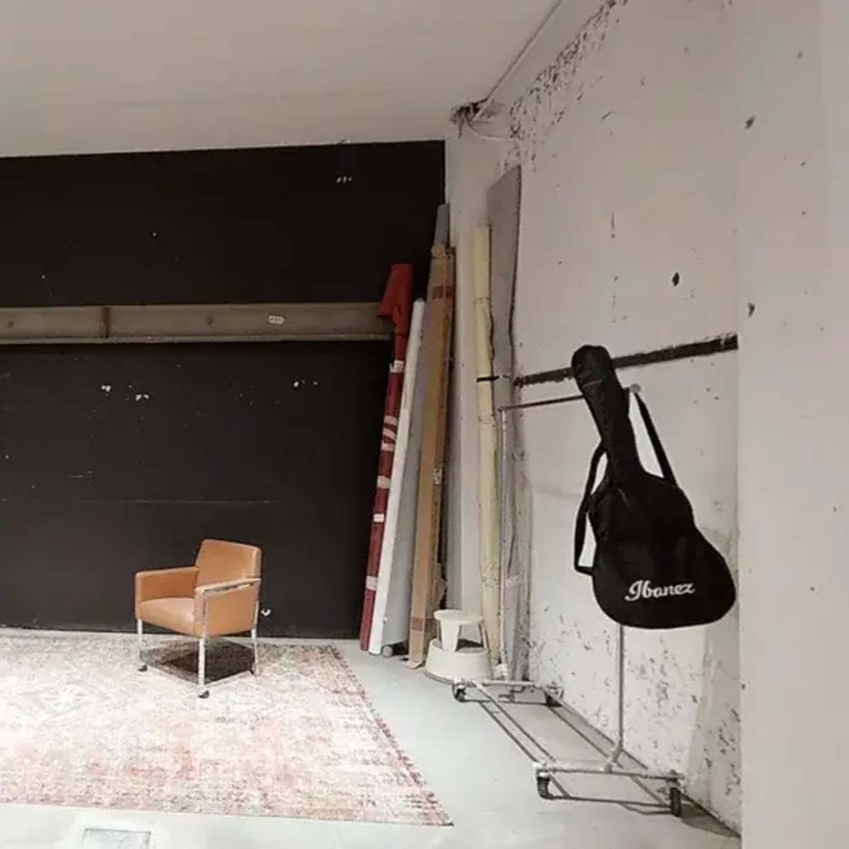 An empty room features a single chair on a rug, a black wall, and a ladder against the wall.