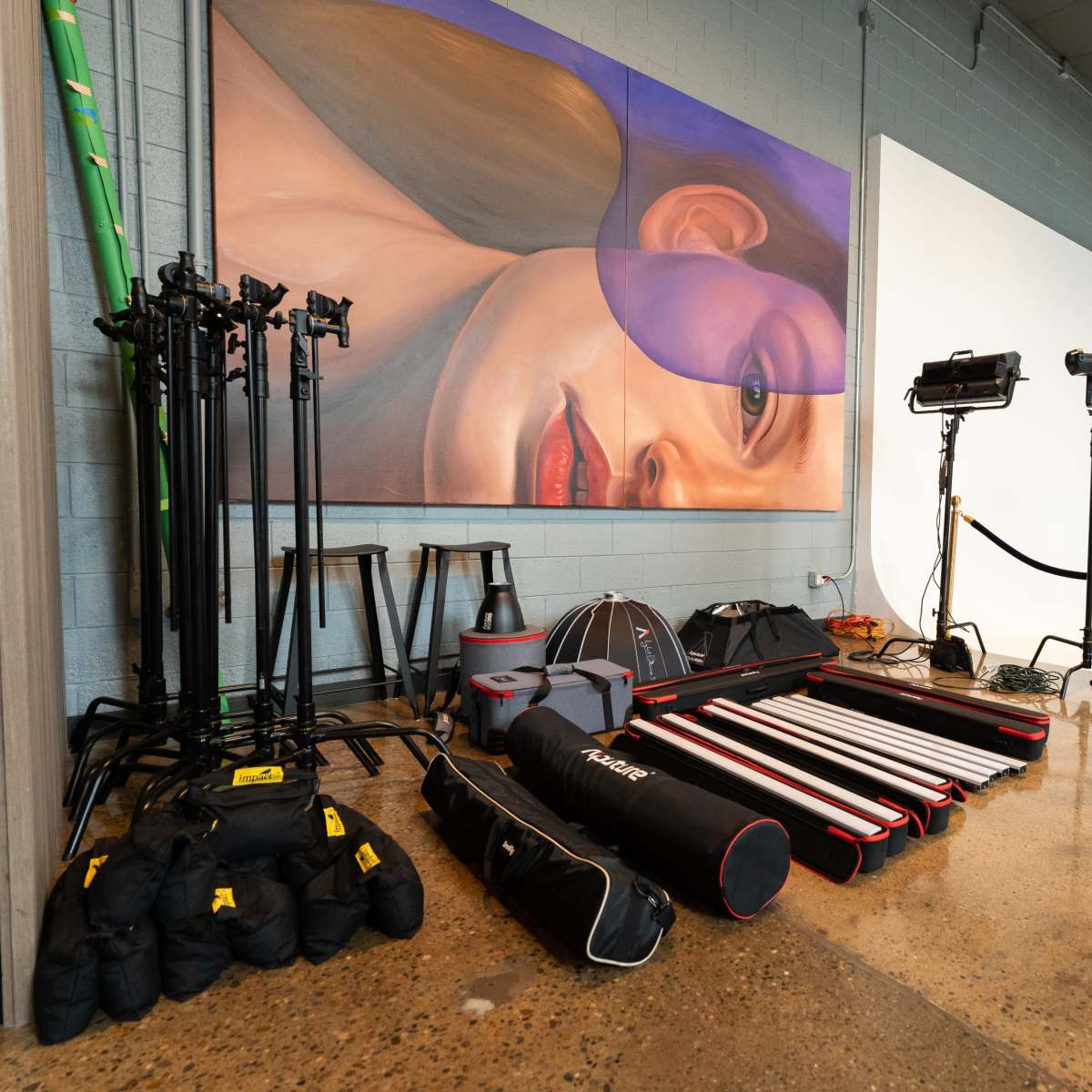 A photography studio is arranged with various lighting equipment and backdrops, alongside a large mural of a woman's face on the wall.