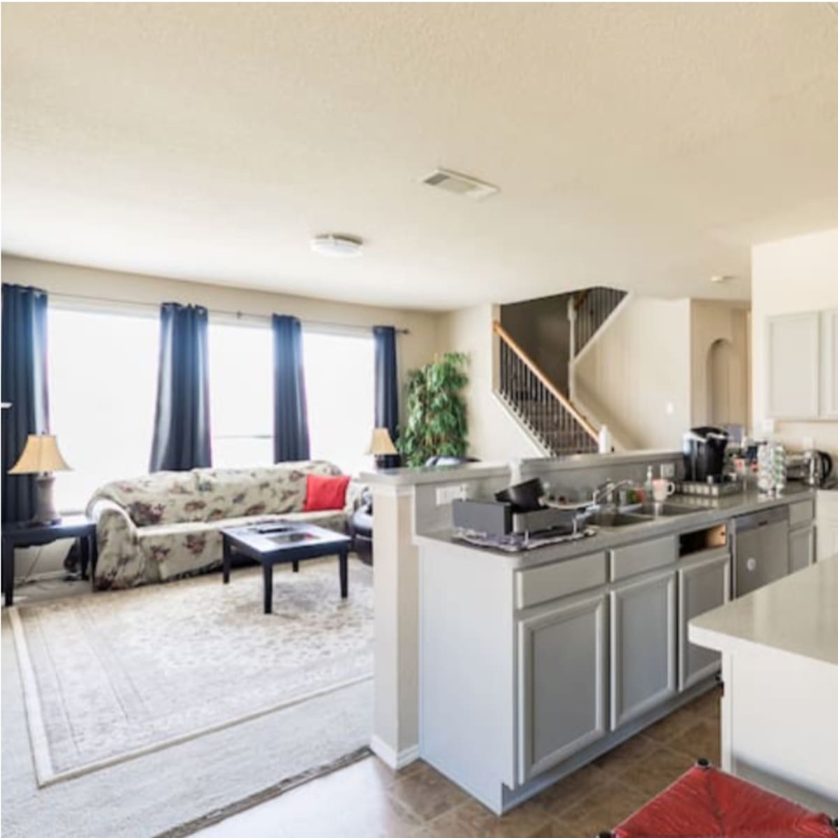 An open-concept kitchen and living area with a staircase in the background and a sofa facing a coffee table.