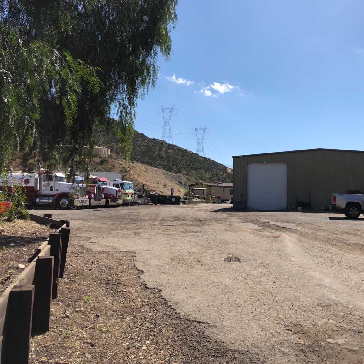A dirt parking lot features a metal building, several vehicles including a fire truck, and power lines in the background.