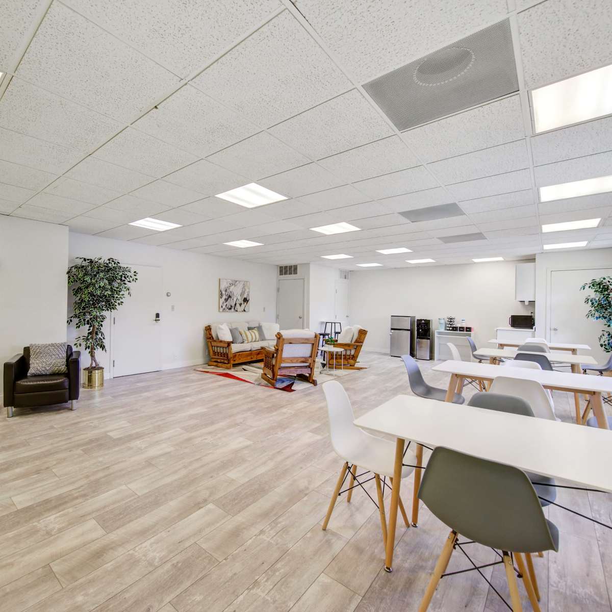 A spacious, well-lit room with seating areas, tables, and a kitchenette.