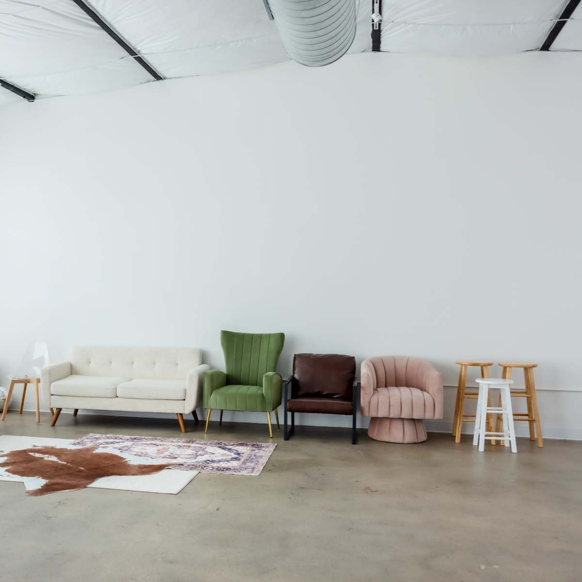 A collection of different styled chairs and couches arranged along a wall in a spacious, well-lit room, with a patterned rug on the floor.