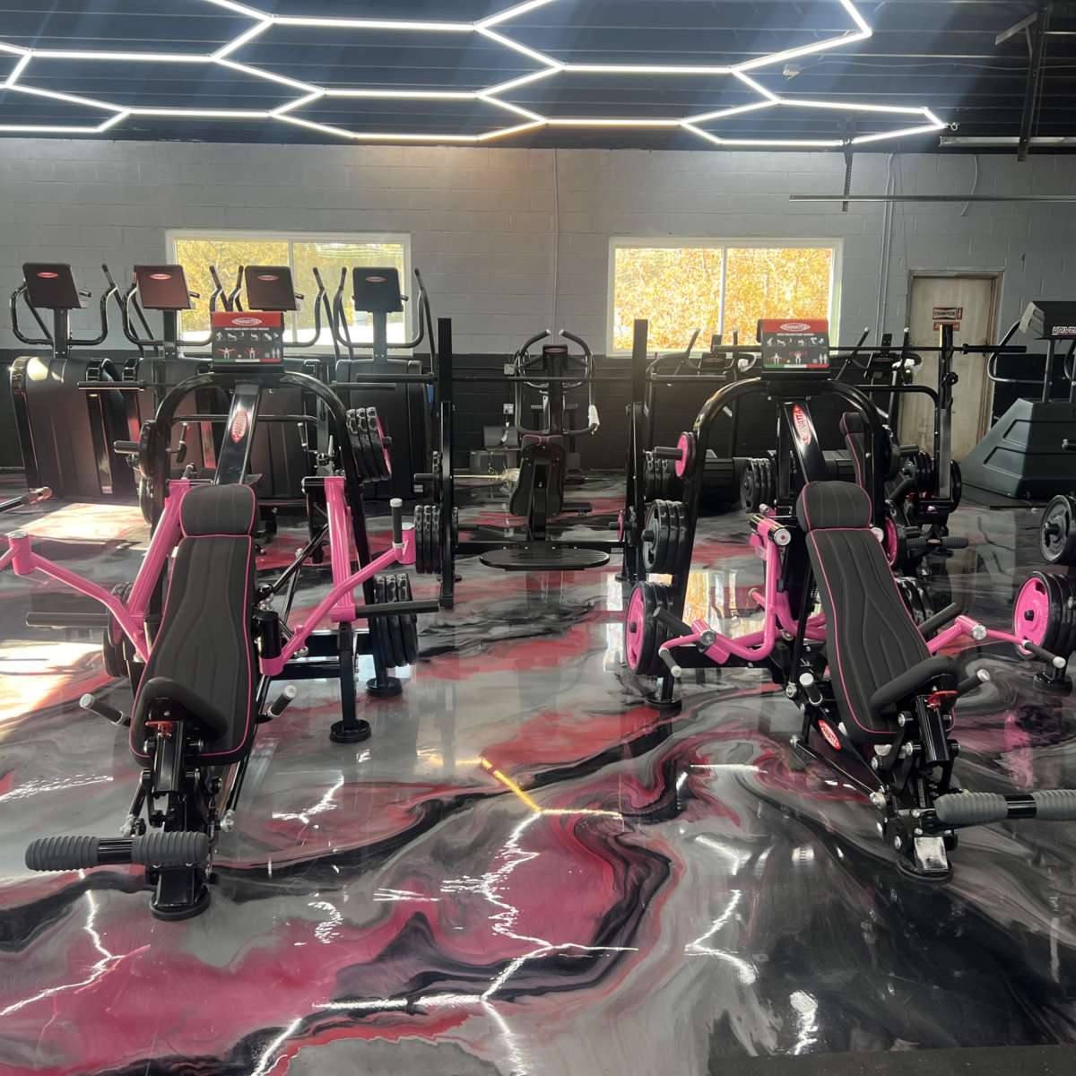 A modern gym interior featuring various exercise machines with black and pink designs on a glossy, marble-patterned floor.