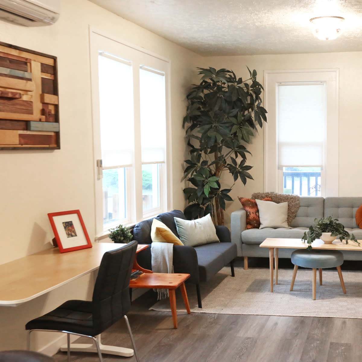 A living room with a gray sofa, a couple of wooden tables, and decorative plants by the window.