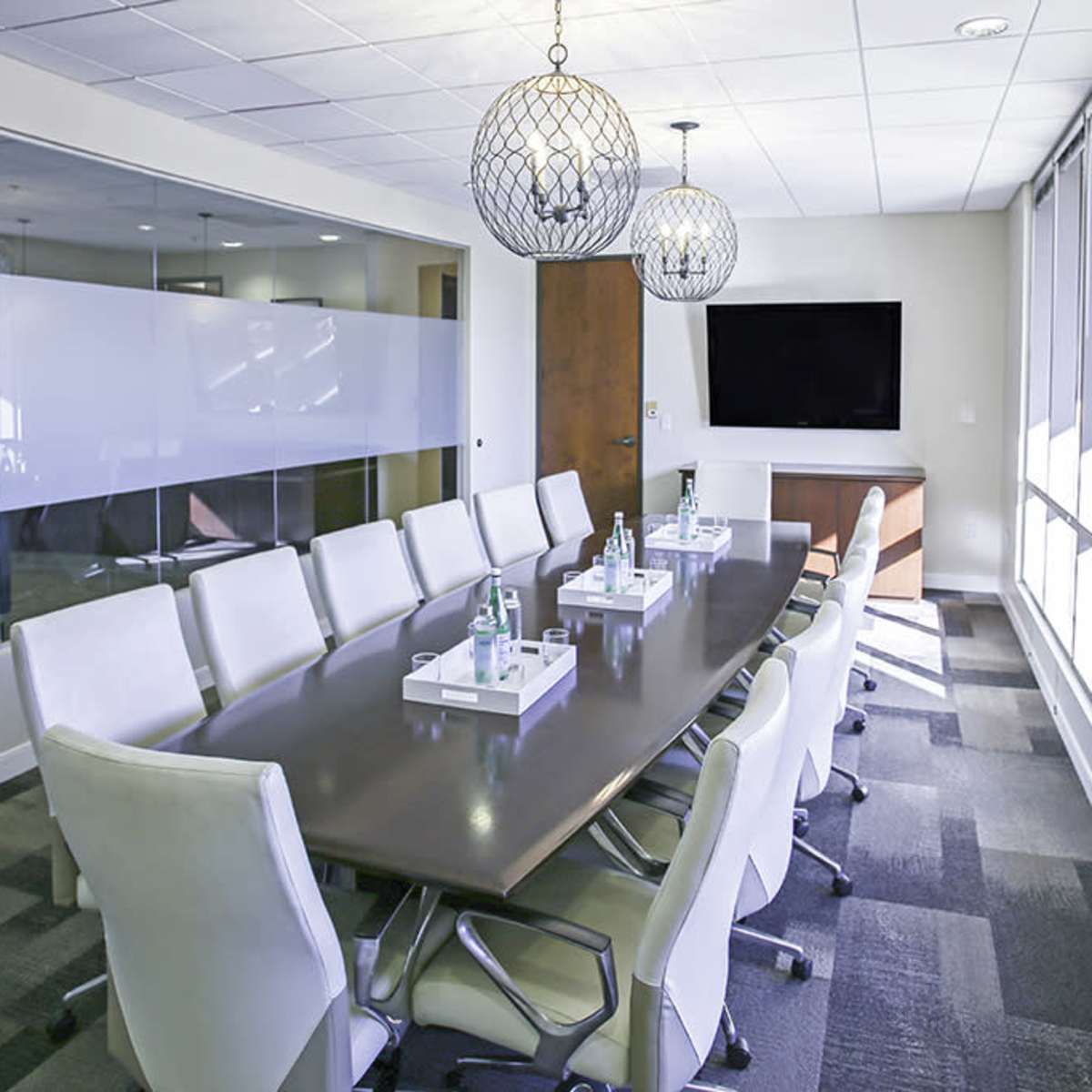 A modern conference room with a long table, white chairs, and large windows letting in natural light.