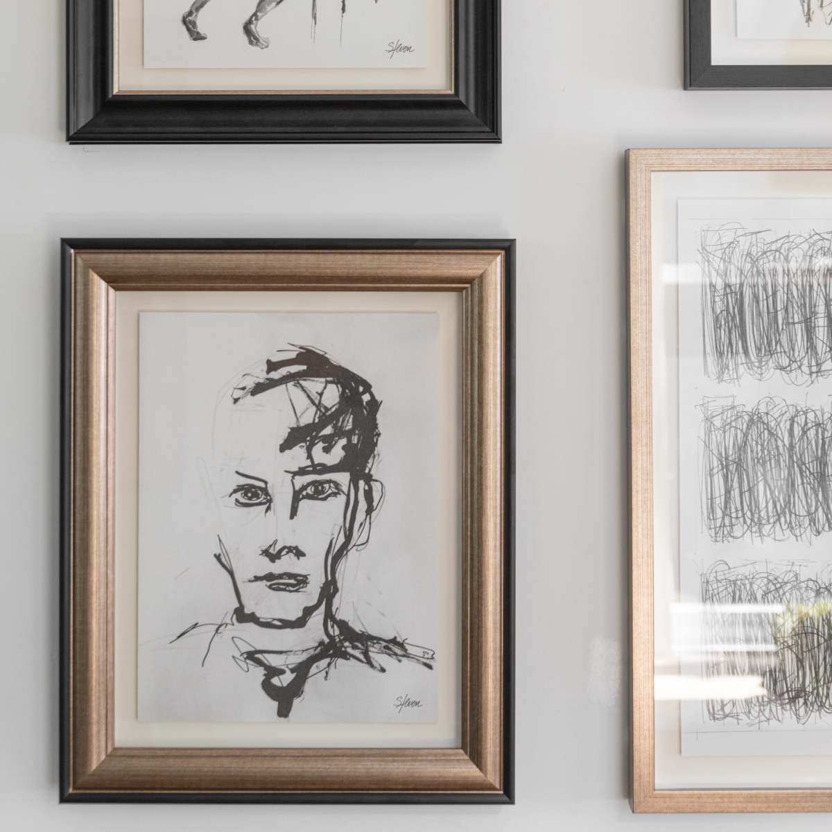 A collection of framed sketches, including a figure leaning on a surface and a portrait of a person, displayed on a wall.