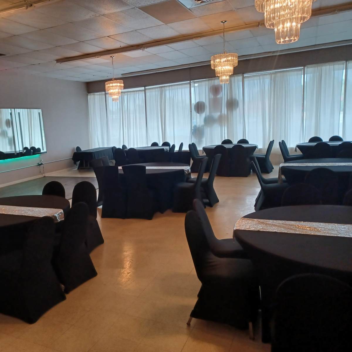 A spacious banquet hall with round tables covered in black cloth and elegant chandeliers hanging from the ceiling.