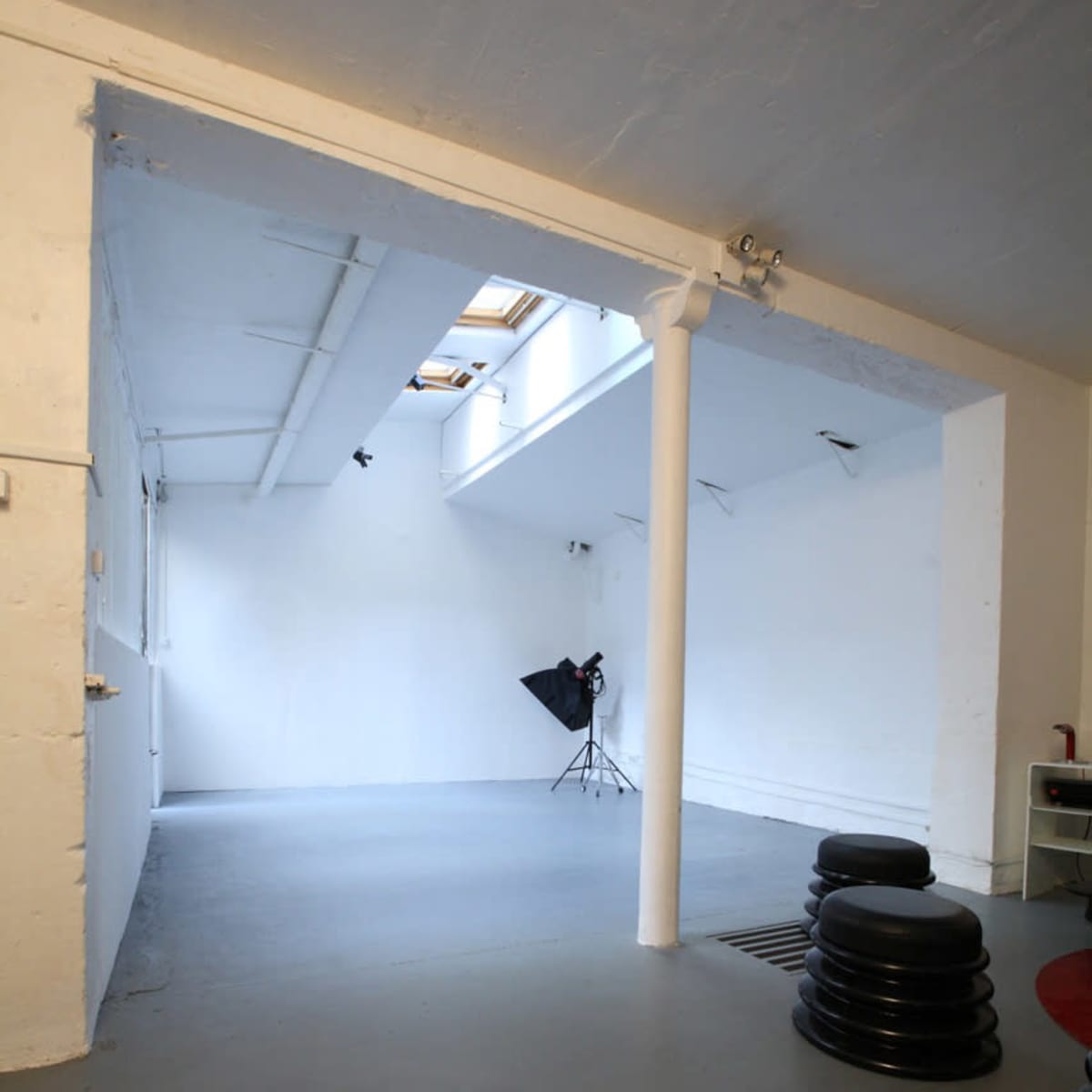 A spacious, well-lit studio with white walls, a gray floor, and a photography backdrop setup in one corner.