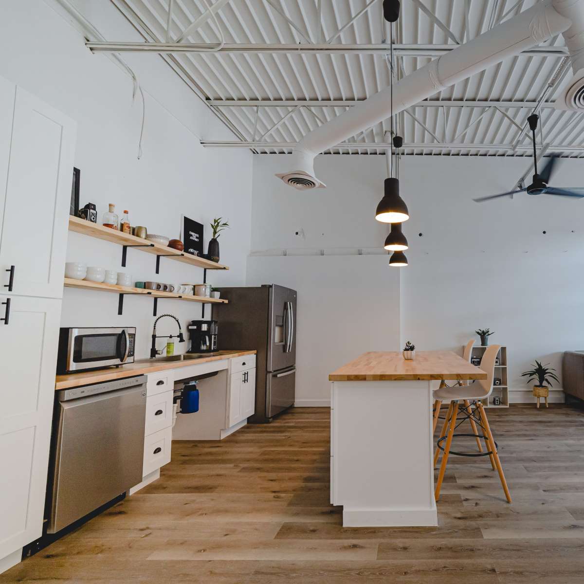 A modern, spacious kitchen and living area features a central wooden island, stainless steel appliances, and large windows leading to an outdoor view.
