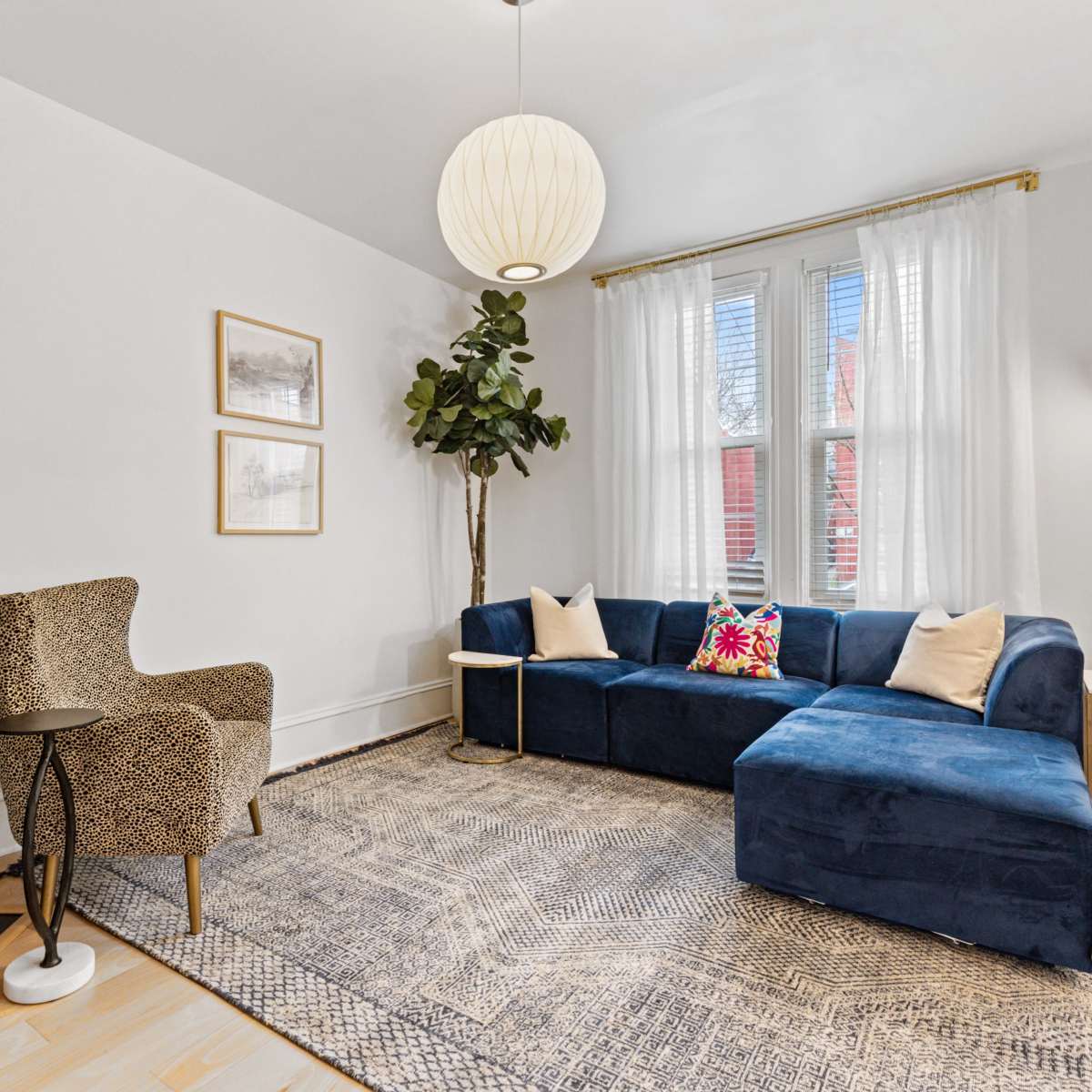 A modern living room features a blue sectional sofa, a patterned chair, a floor lamp, and a television mounted on the wall.