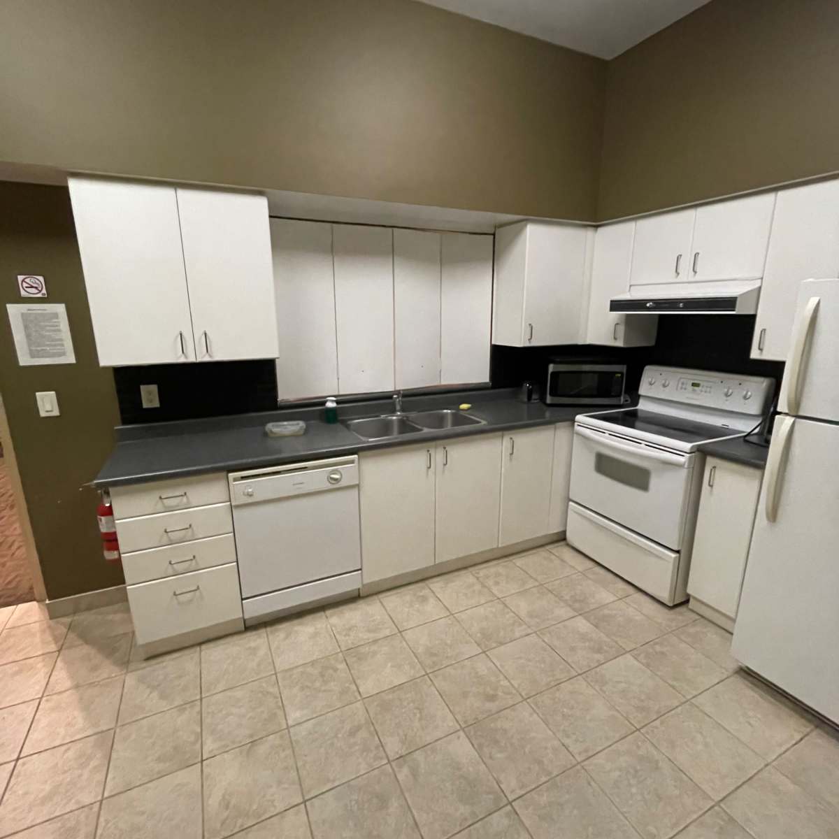 A small kitchen features white cabinetry, a black countertop, and standard appliances including a dishwasher, microwave, and stove.