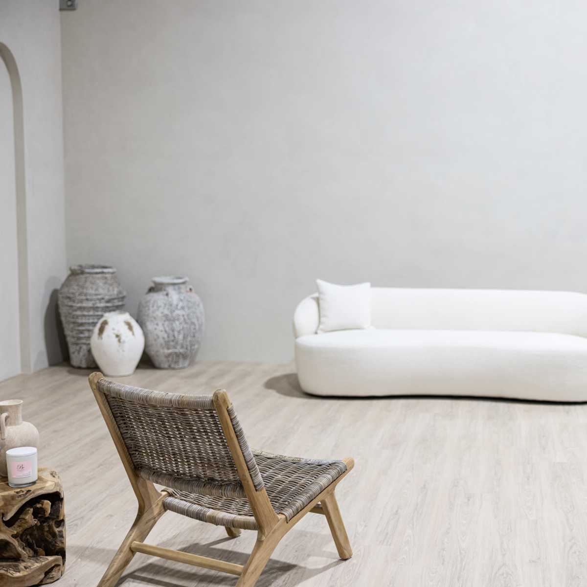 The scene features a minimalist room with a white curvy sofa, a wooden chair, and decorative vases against a light-colored wall.