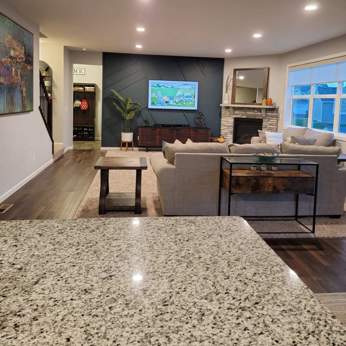 A modern living room featuring a sectional sofa, a television mounted on a textured wall, and a coffee table positioned in front of a stone fireplace.