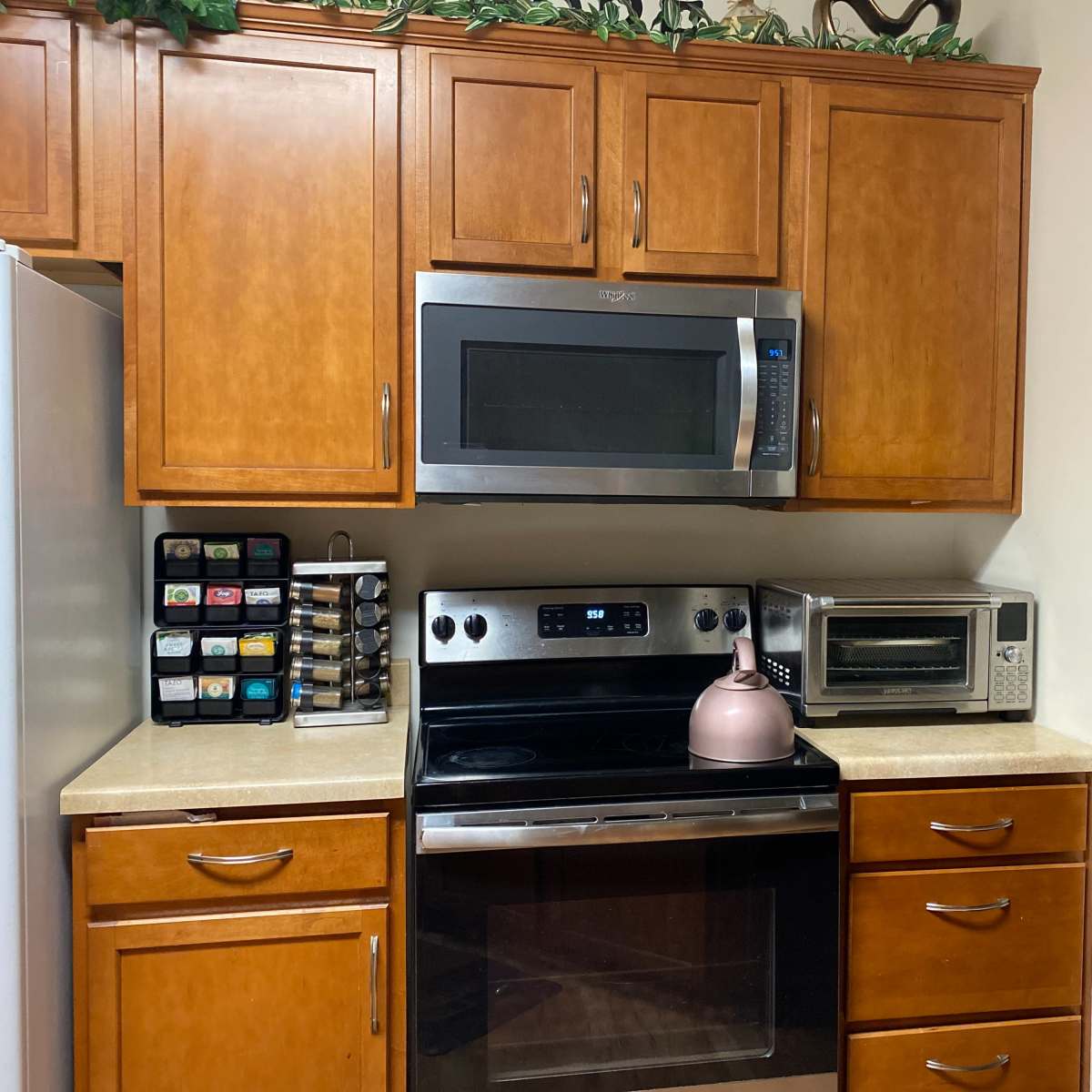 A kitchen with wooden cabinets, a microwave, an oven, an electric kettle, and a countertop appliance.