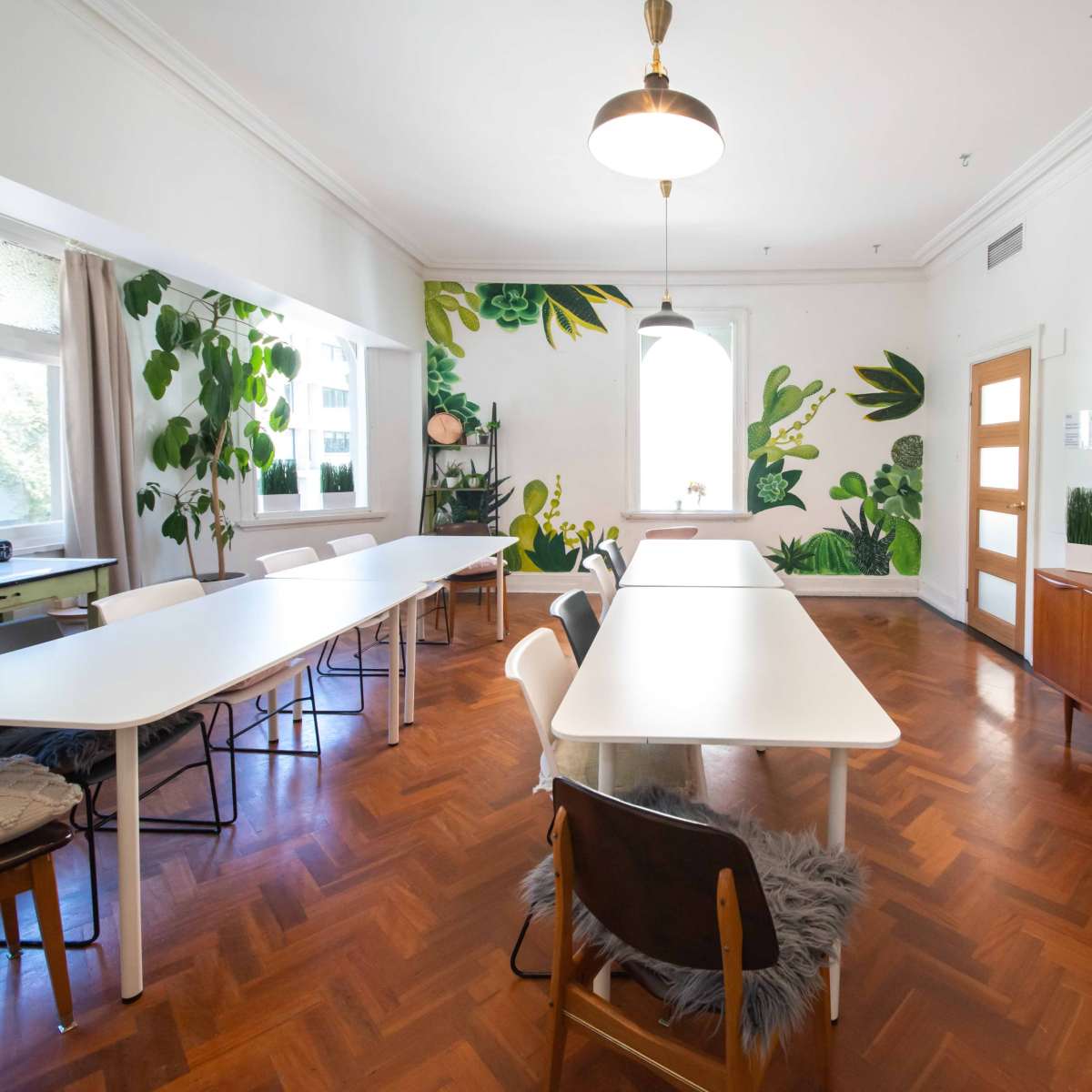 A bright room with large tables, wooden flooring, and green plant-themed wall decorations.