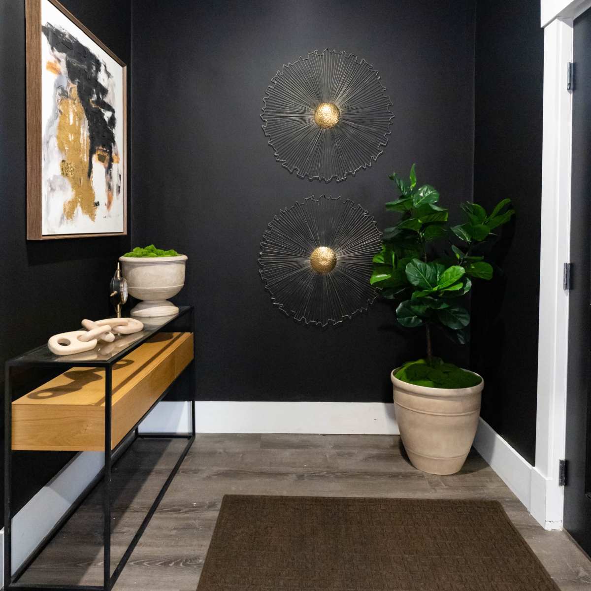 A modern hallway featuring a dark wall, a wooden console table with a decorative object, two circular wall sculptures, and potted plants.