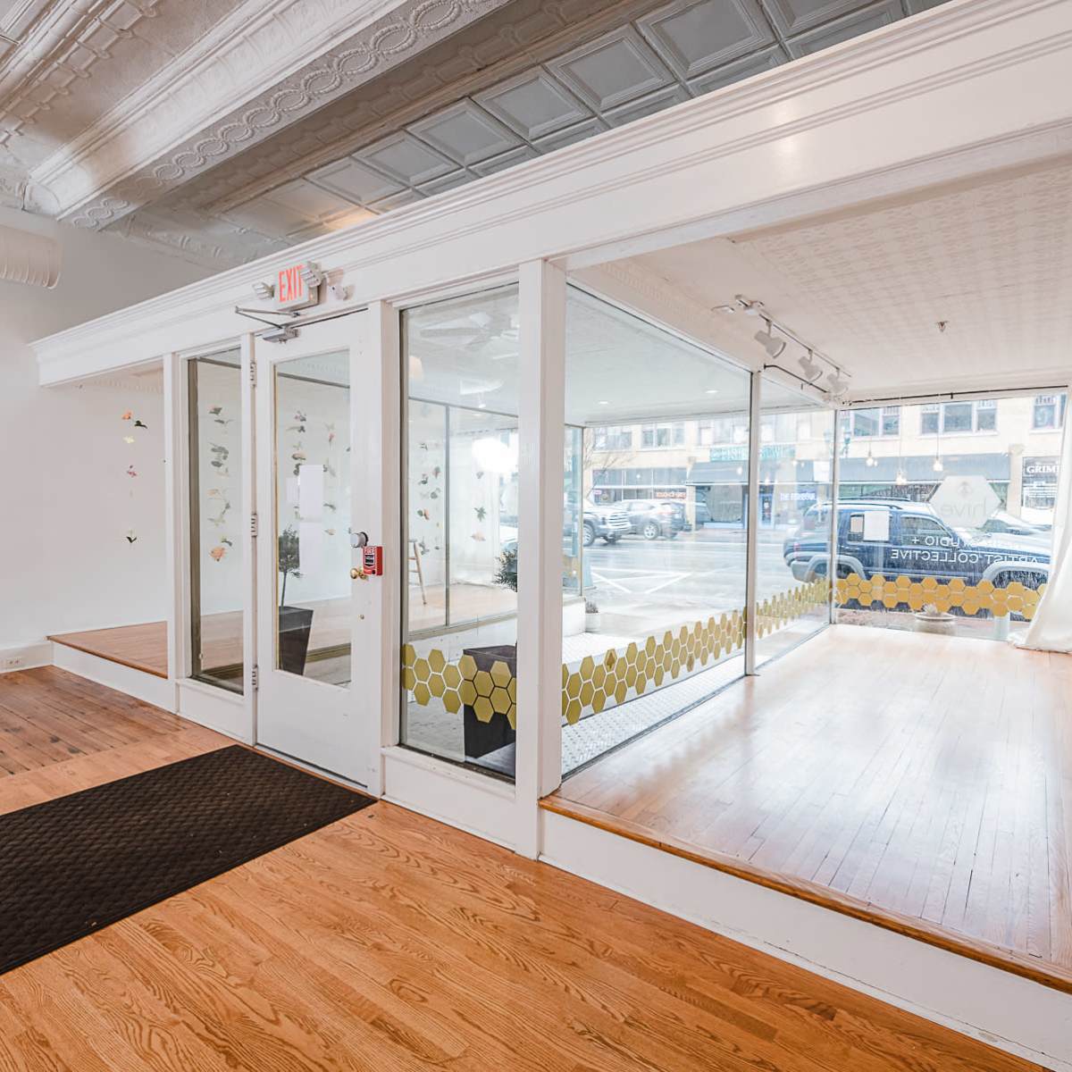 A bright, modern interior of a shop with wooden flooring, large glass windows, and a small display area.