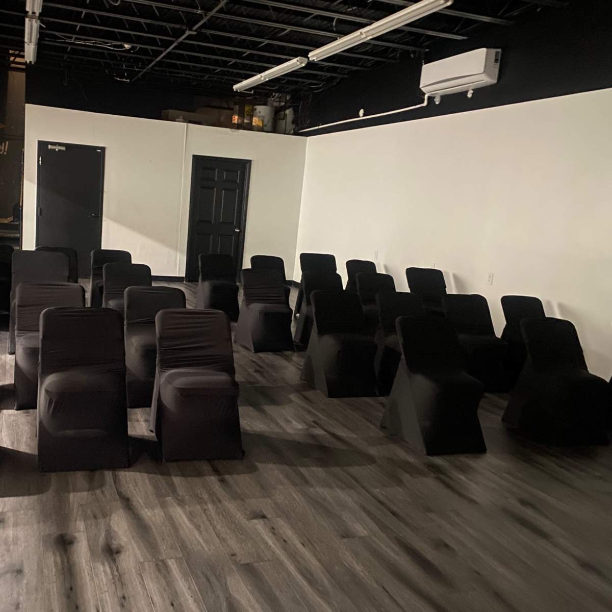 A room arranged with black-covered chairs facing a blank wall, on a wooden floor.