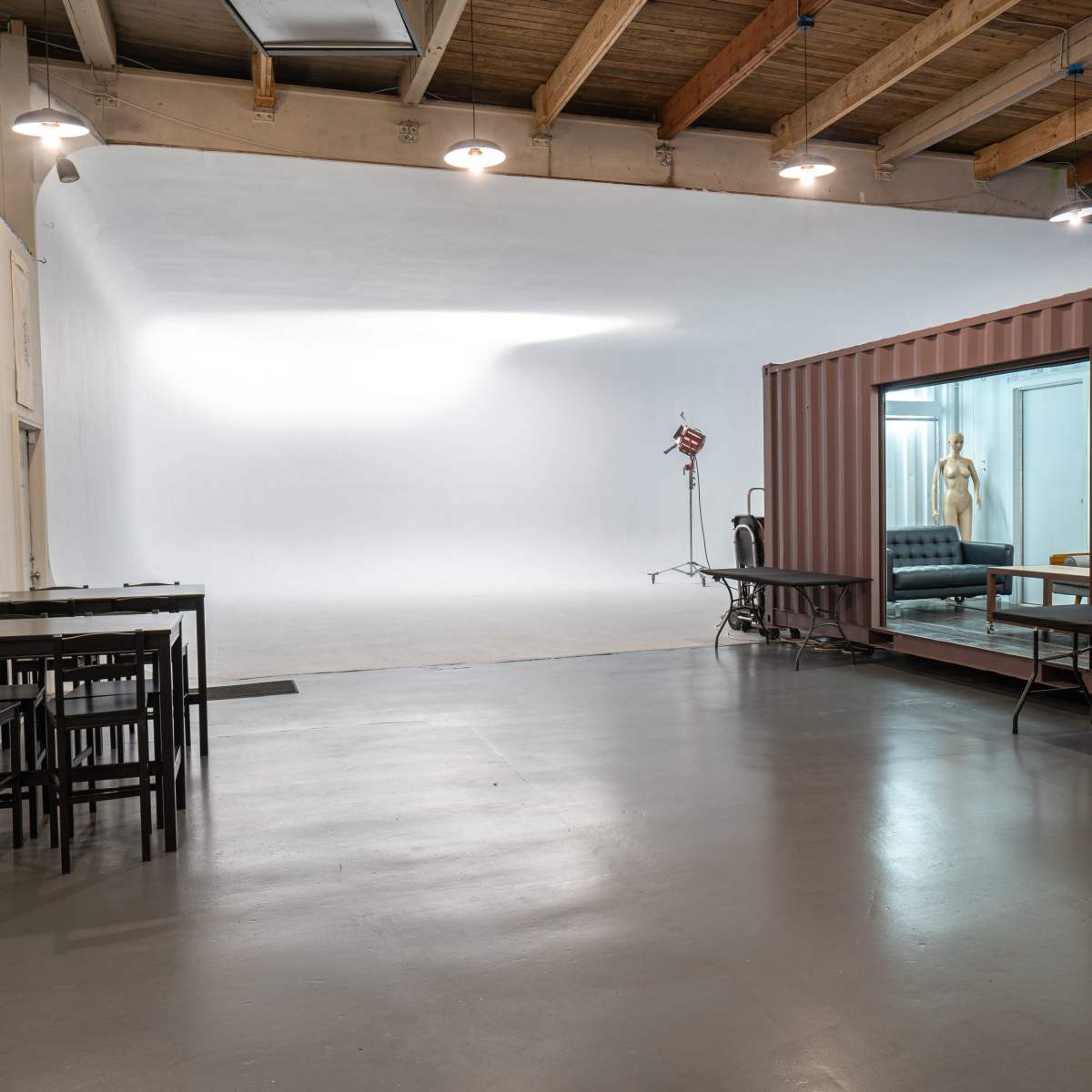A spacious studio with a white backdrop, a black couch, a mannequin, and a shipping container used as a workspace.