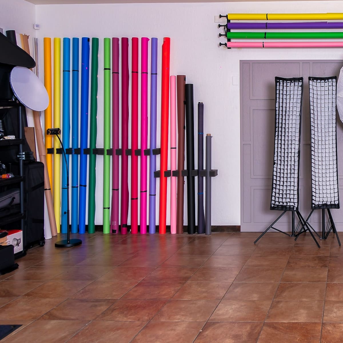 A photography studio setup with various colored backdrops, reflectors on stands, and equipment arranged along the walls.
