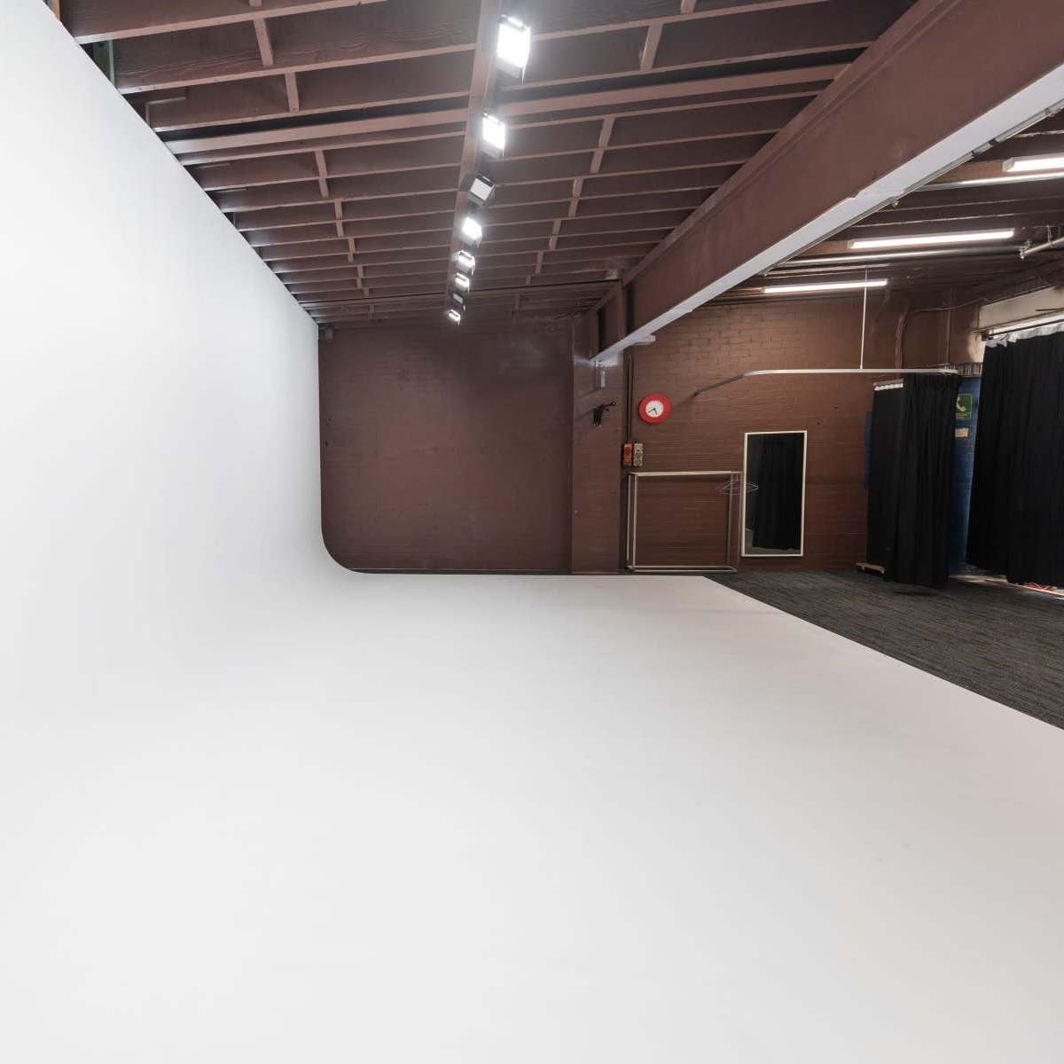 A spacious, empty studio with a seamless white backdrop and overhead lighting.