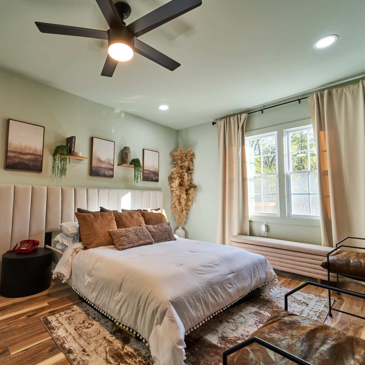 The bedroom features a light green color scheme with a bed, a nightstand, two windows, and decorative wall art.