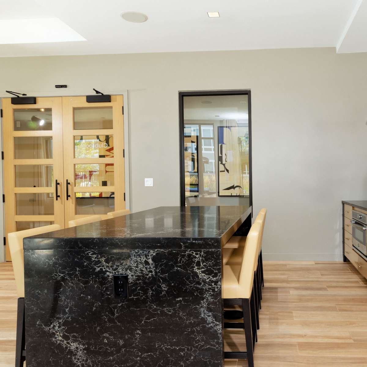 A modern kitchen featuring a large black countertop with beige seating and a light-colored wall with pendant lighting.