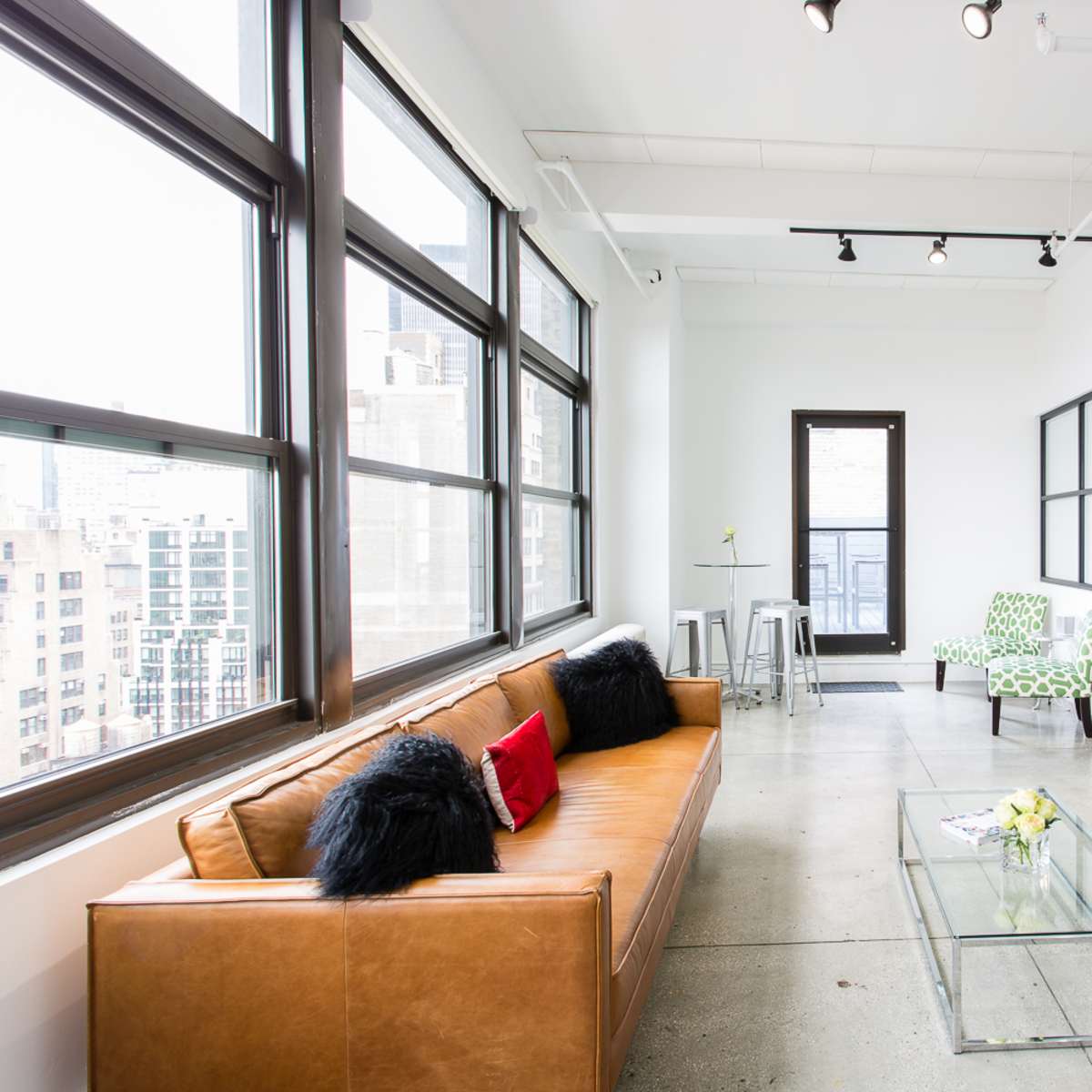 A modern, open-concept living space with large windows, a leather sofa, a glass coffee table, and a dining area featuring wooden chairs.
