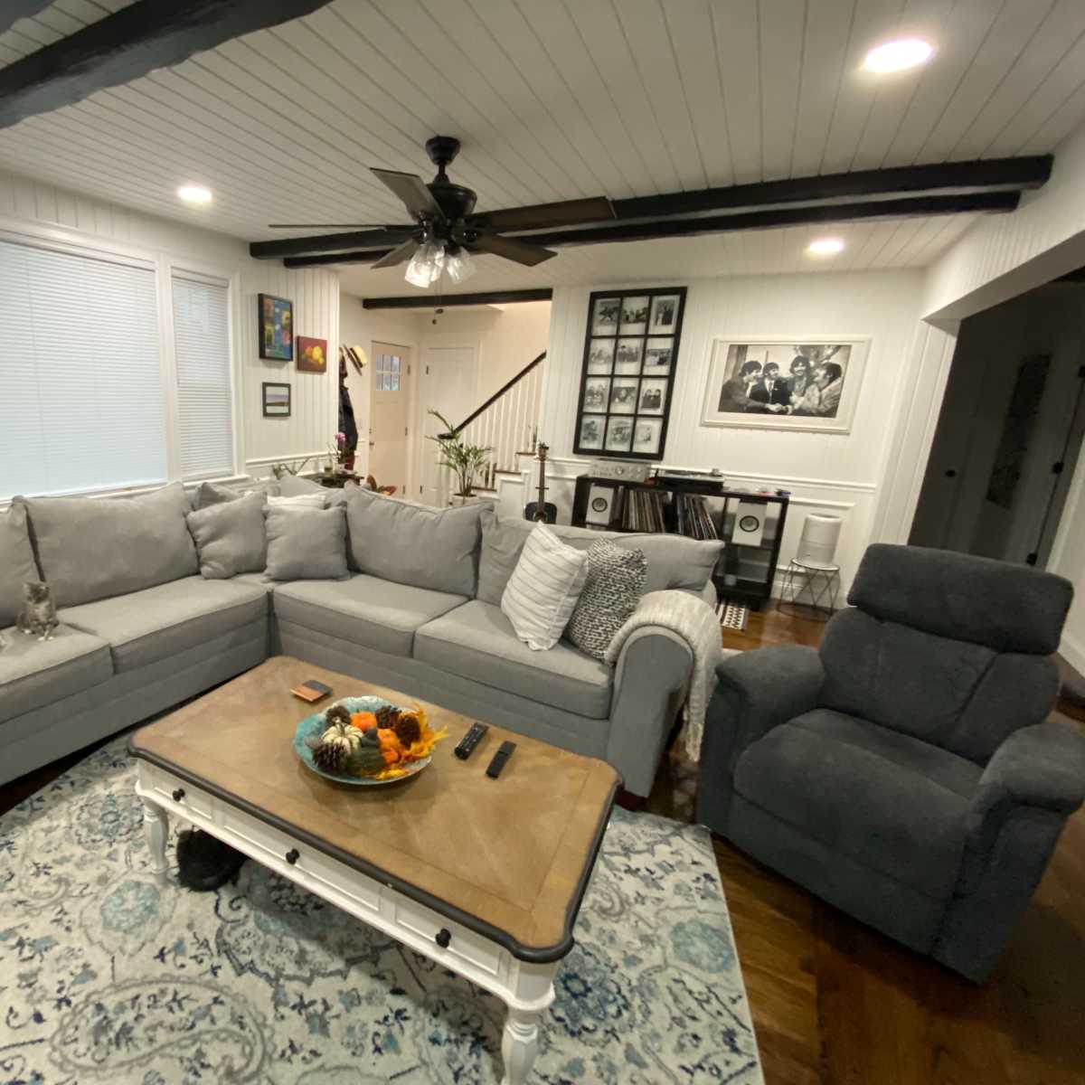 A living room with a gray sectional sofa, a wooden coffee table, and a recliner chair, all arranged around an area rug on polished hardwood floors.