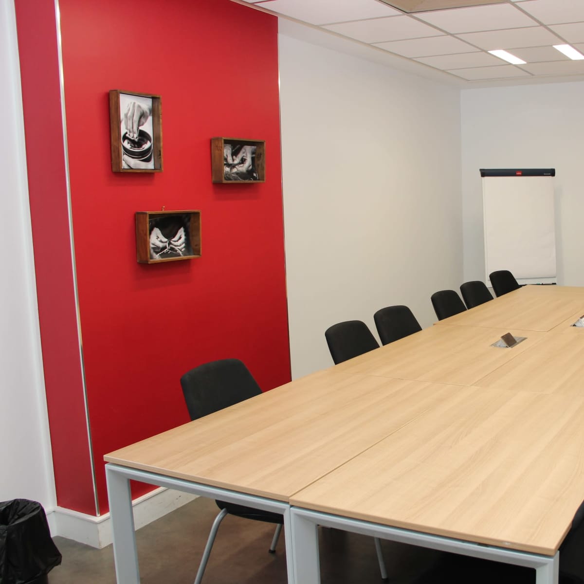 A modern conference room with a long wooden table surrounded by black chairs, red accent walls, and a whiteboard on one side.