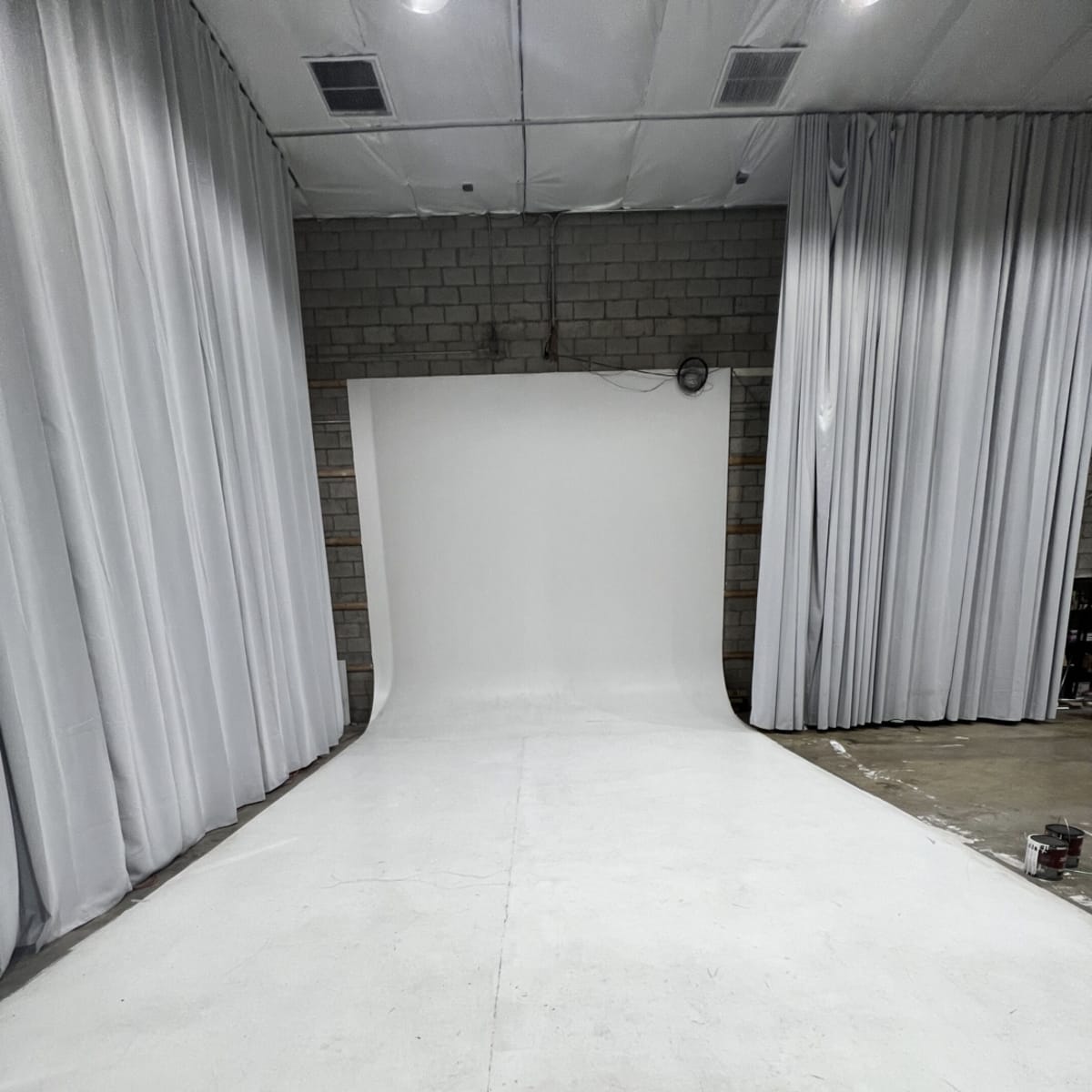 A photography studio features a seamless white backdrop with draped white fabric on either side.
