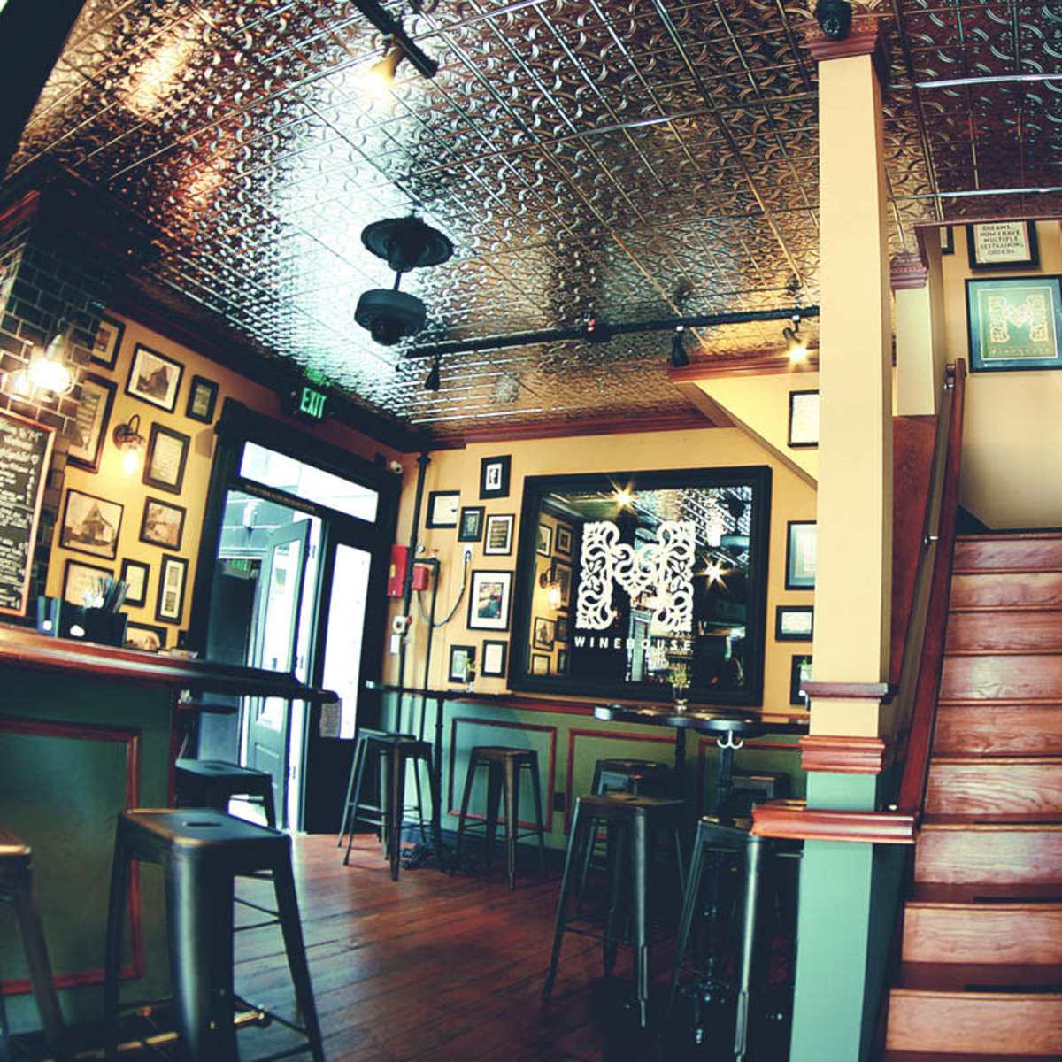 The interior of a bar or pub with hardwood flooring, a staircase on the right, and various framed pictures on the walls.
