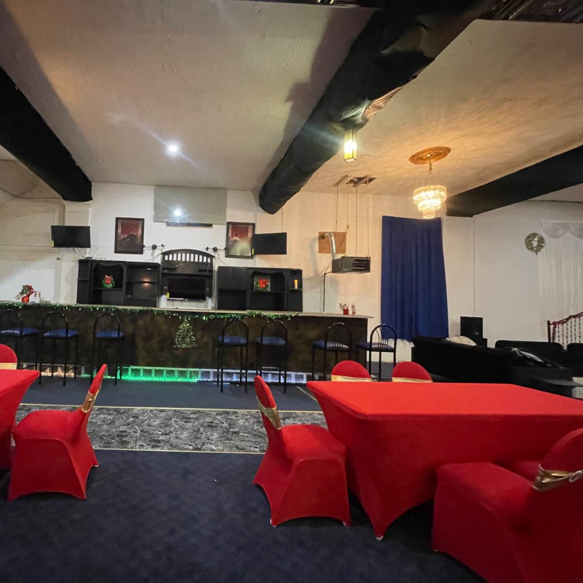The interior features a bar area with a green lit counter, surrounded by red tables and chairs, under softly glowing lights.