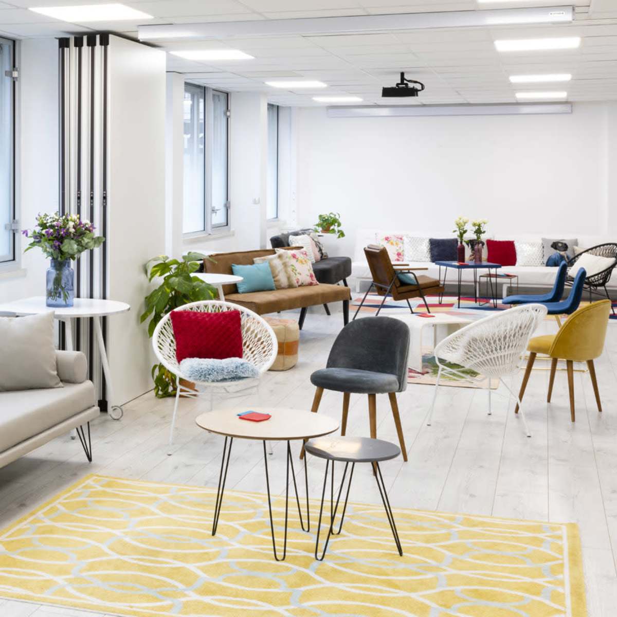 A modern office lounge features a variety of seating options, decorative plants, and large windows allowing natural light.