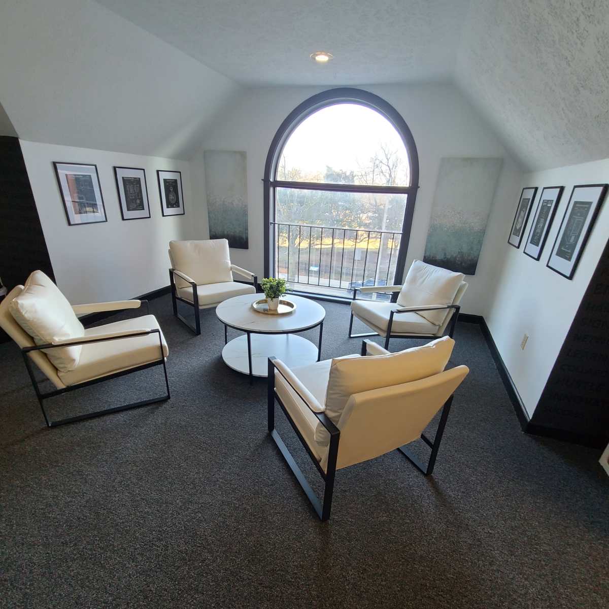 A sitting area with four chairs arranged around a round coffee table, featuring large windows overlooking a scenic view.