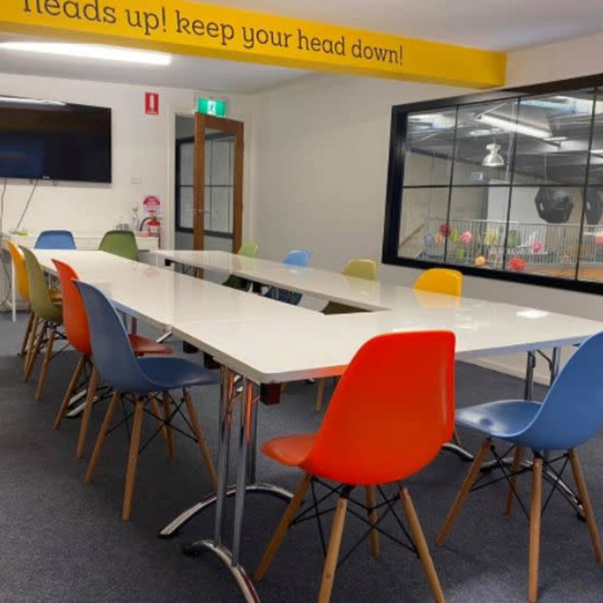 A modern conference room features a long white table surrounded by colorful chairs in orange, blue, and green.